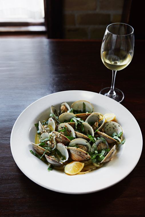 Clams in a herbed white wine broth beside a glass of white wine