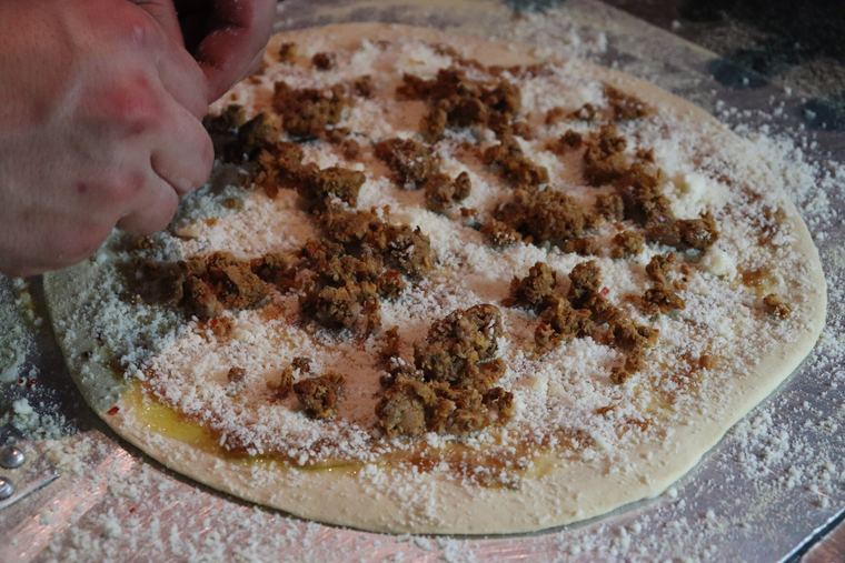 A cook's hand grating cheese over a raw round of pizza dough dusted with flour