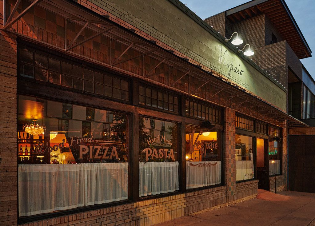 The Vespaio Ristorante storefront on South Congress Avenue at dusk, warm light behind windows lettered PIZZA and PASTA