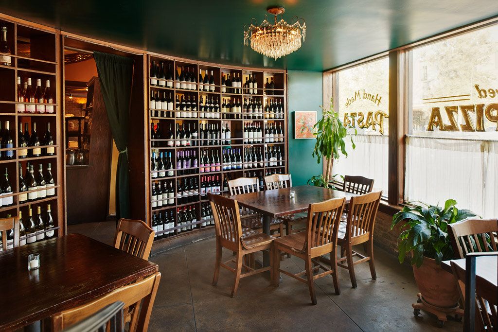 The Vespaio front room: green walls, wine bottles shelved floor to ceiling, and a small table set for two